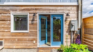 A wooden house with a blue door, a window, and a small garden area with plants. - Charming Urban Cottage in Cap Hill (Seattle)