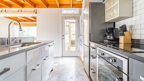 A modern kitchen with a wooden ceiling, stainless steel appliances, and a view to the outside. - Charming Urban Cottage in Cap Hill (Seattle)