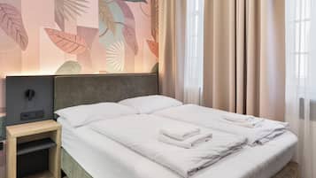 Una cama bien tendida con ropa blanca y toallas, una mesita de noche con una lámpara, y una pared con un diseño de hojas.