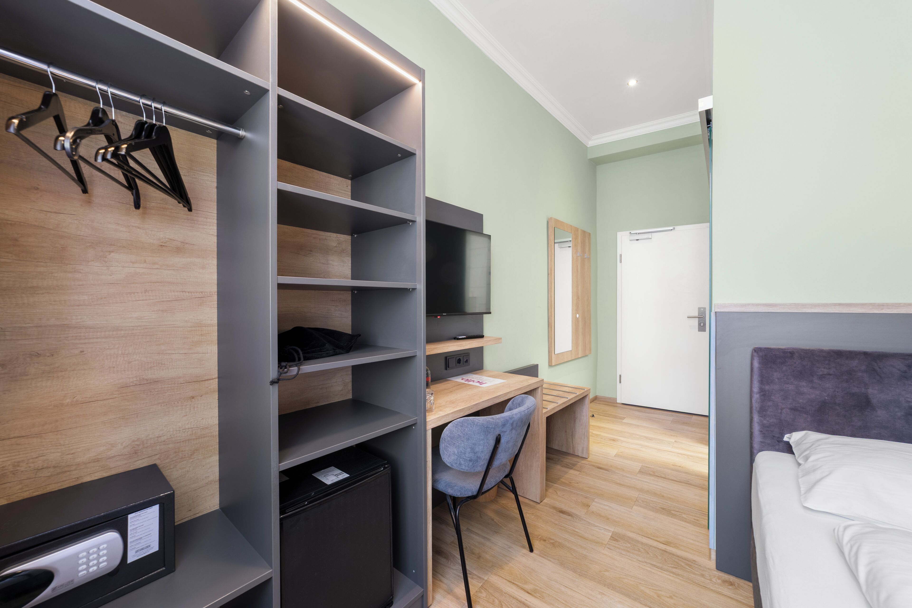 Una habitación moderna con cama, escritorio, silla, armario y televisor.
