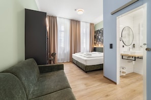 Een slaapkamer met een bed, een stoel, een nachtkastje, een spiegel en een badkamer met een wastafel en toilet.