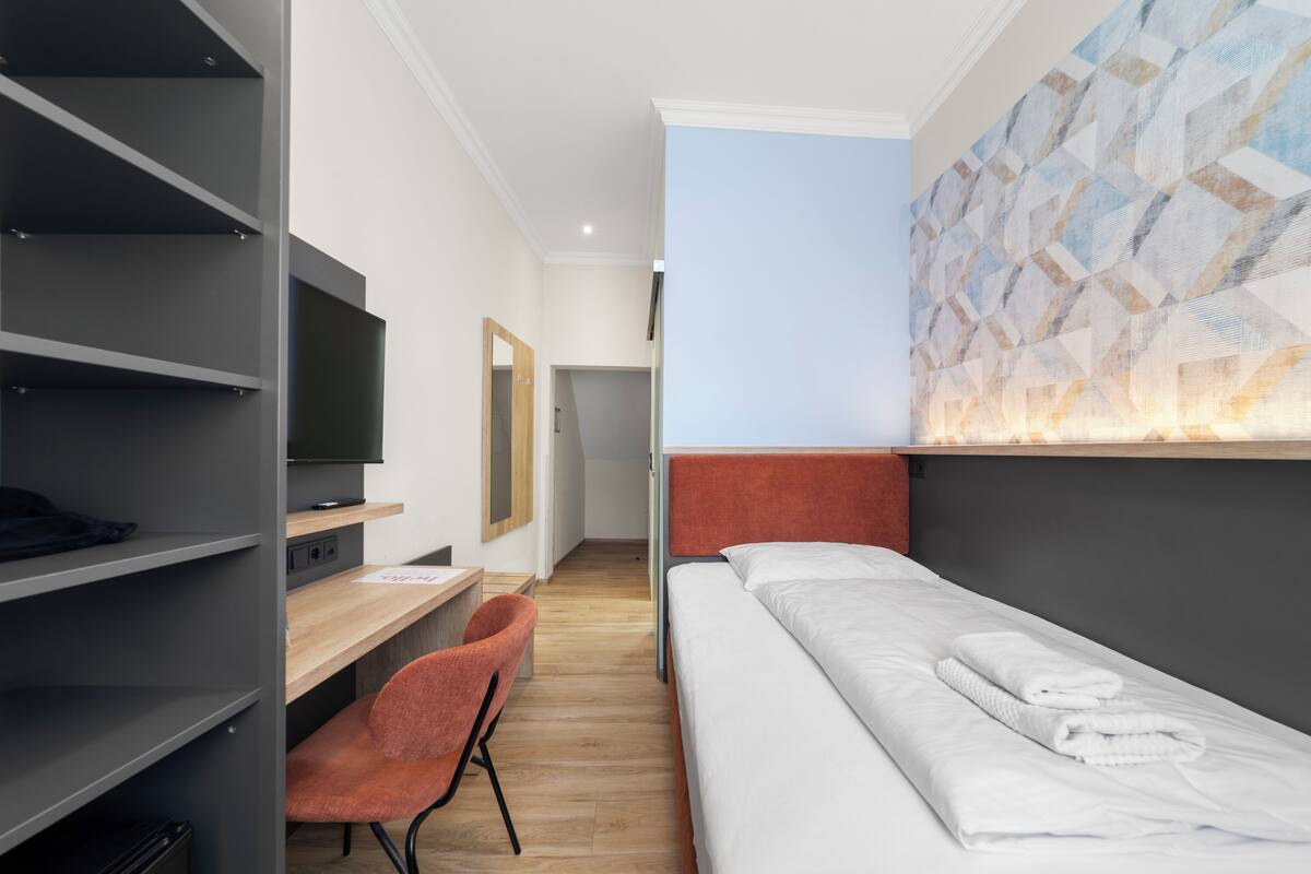 Une chambre d’hôtel équipée d’un lit, d’un bureau, d’une chaise, d’une télévision et d’un mur orné d’un motif géométrique.