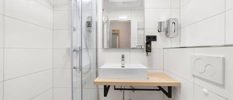 A modern bathroom with a glass shower enclosure, a white sink with a wooden countertop, and a mirror above the sink.