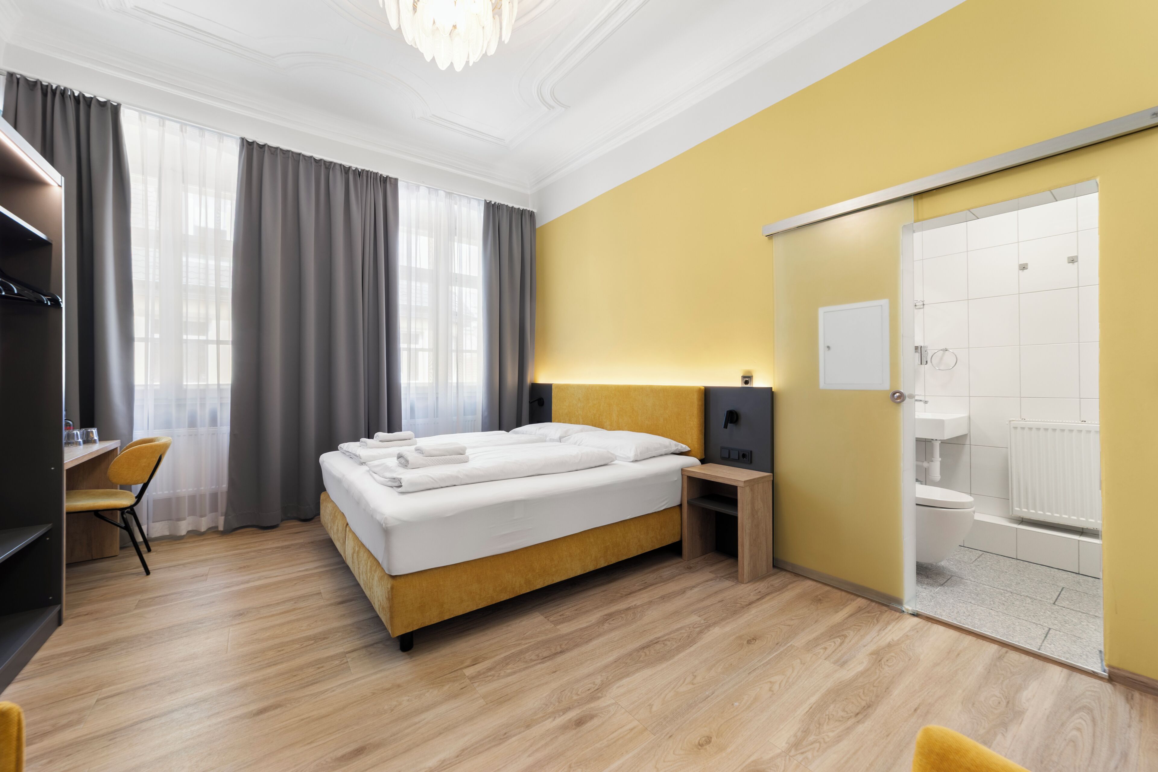 A hotel room with a bed, desk, chair, and a bathroom with a toilet and sink.