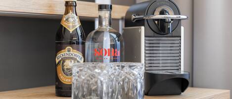 A bottle of Reckendorfer Keller-Pilsner, a glass of Sona Design Broke, and a Nespresso machine on a wooden surface.