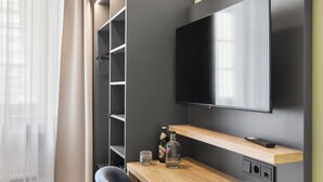 A modern room with a flat-screen TV mounted on the wall, a wooden desk with a bottle and glass, and a chair. - Sona Design Rooms City Center (Bamberg)