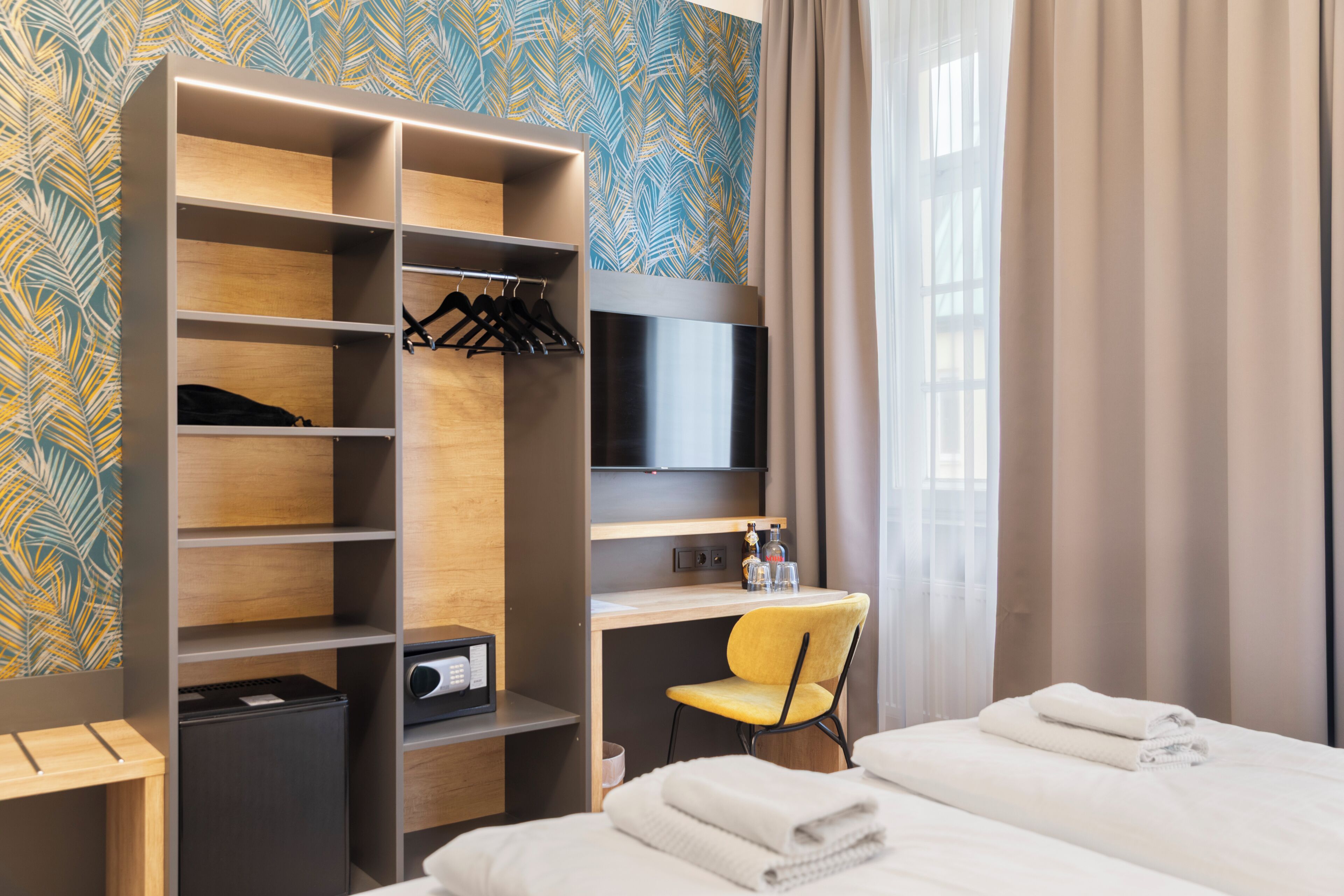 Quarto de hotel com roupeiro, uma escrivaninha com cadeira, cama e televisão.