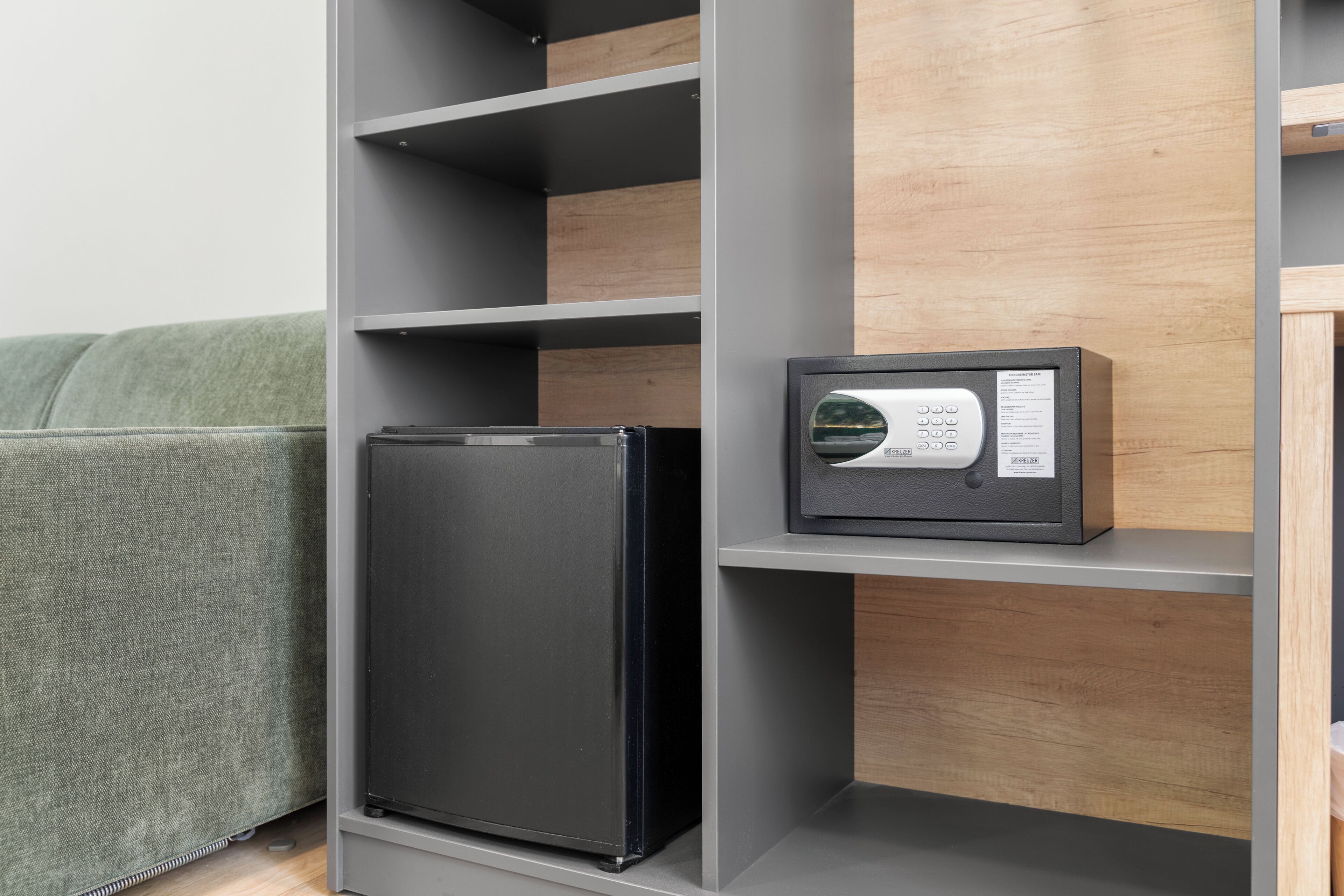 Una cocina moderna con un refrigerador y microondas integrados en color negro, muebles grises y un sofá tapizado en verde.