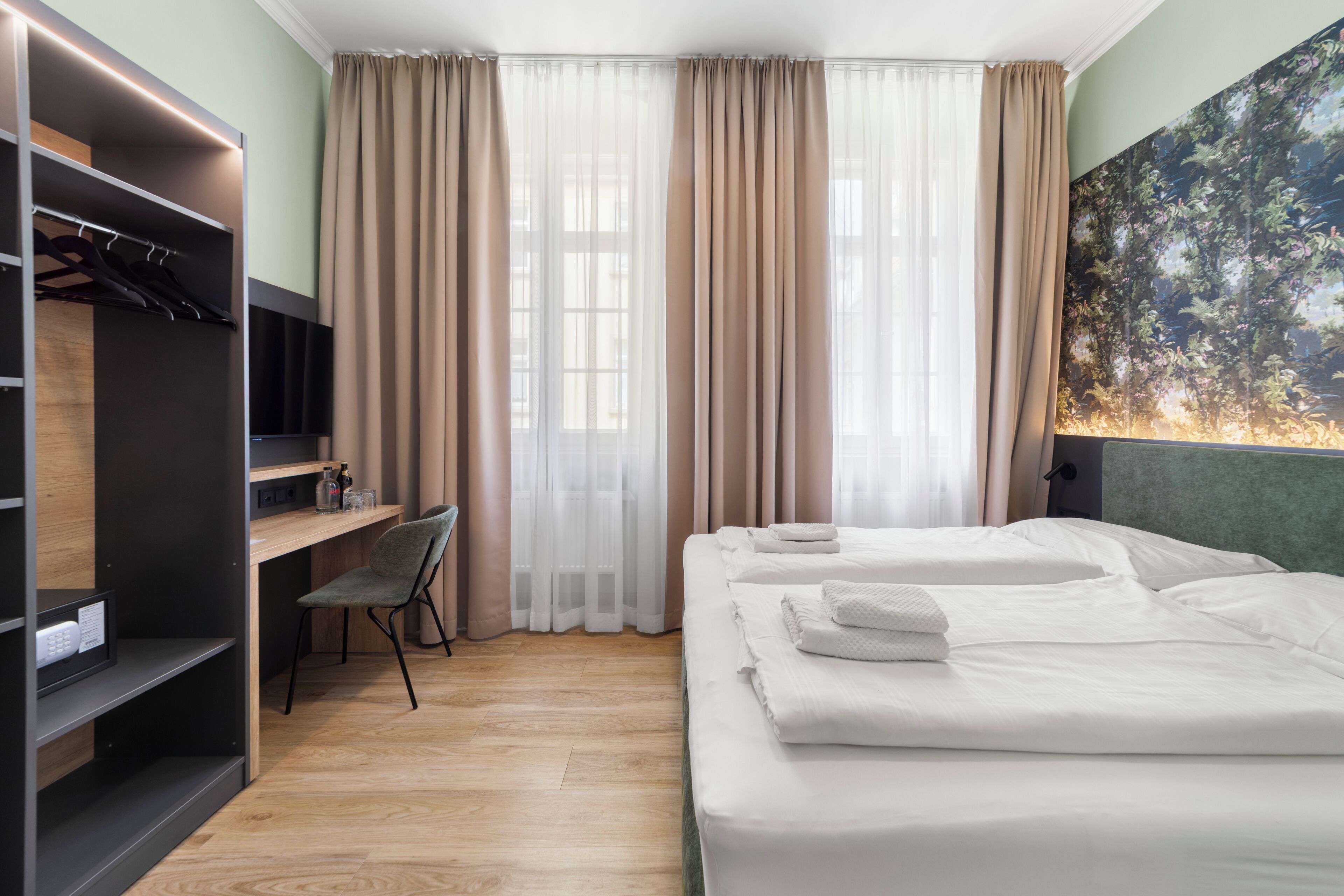 A hotel room with a bed, a desk, a chair, a wardrobe, and a large window with curtains.