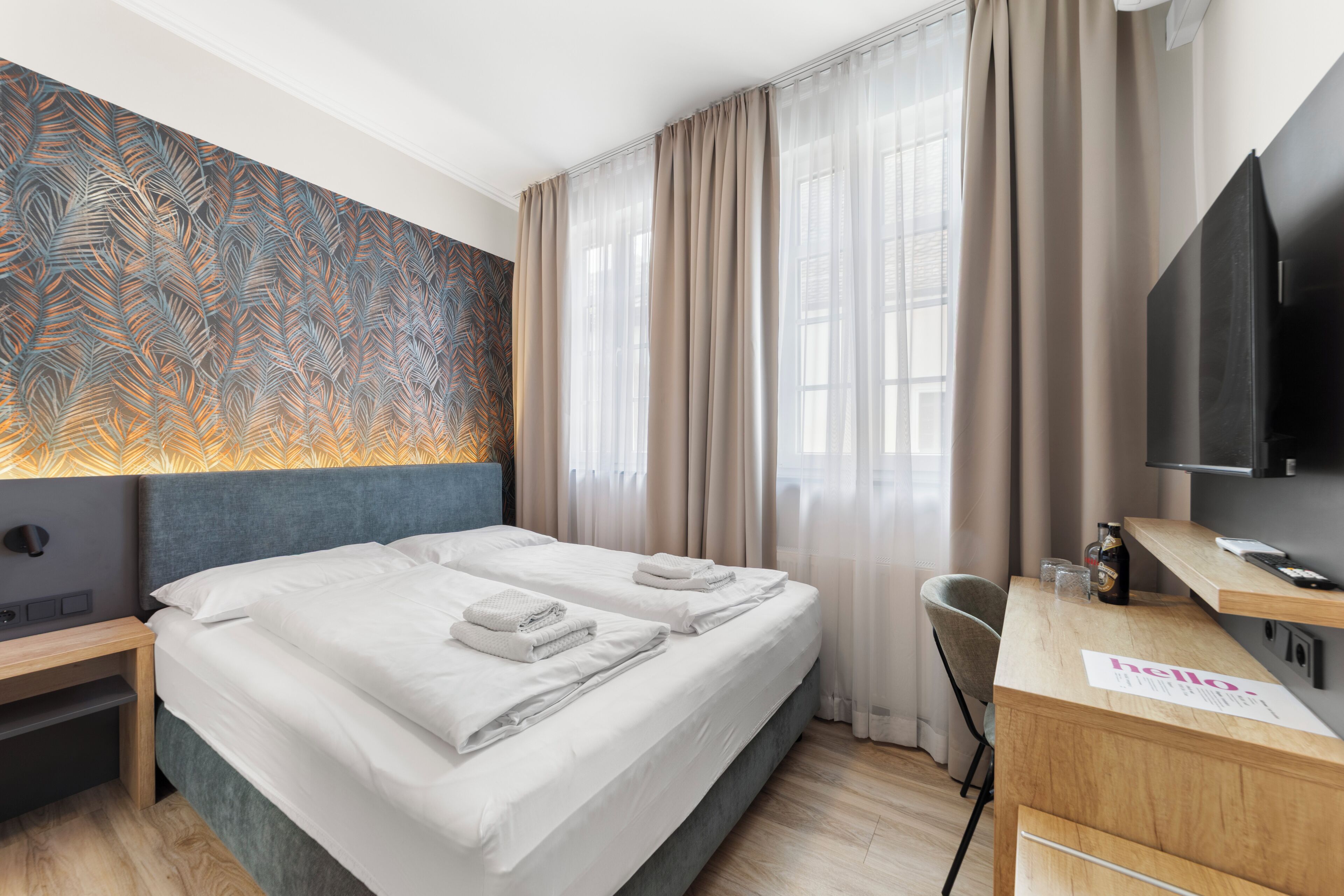 A hotel room with a bed, a desk, a chair, a TV, and a patterned wall.