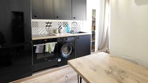 Ett kompakt kök med svarta skåp, en tvättmaskin och ett matbord i trä.