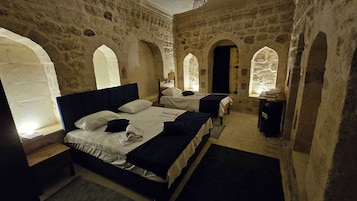 Una habitación con una cama grande, dos camas más pequeñas, paredes de piedra y ventanas en arco.