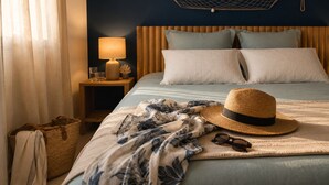 A neatly made bed with a blue and white floral blanket, a straw hat, and sunglasses on the bed.