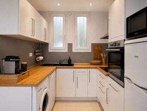Een moderne keuken met witte kastjes, een ingebouwde oven, een magnetron en een wasmachine.