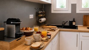 A kitchen with a toaster, bread, croissants, a coffee maker, a fruit bowl, and a bottle of orange juice.