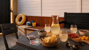 A table set outdoors with a pitcher, glasses, snacks, and playing cards.