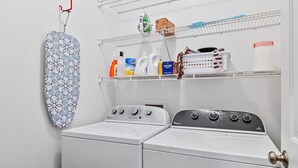 Una sala de bugaderia amb dues rentadores blanques Whirlpool, un tendal i prestatges amb productes de neteja.