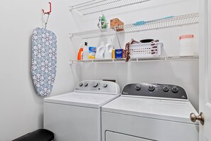 Uma lavanderia com duas máquinas de lavar Whirlpool brancas, um varal e prateleiras com produtos de limpeza.