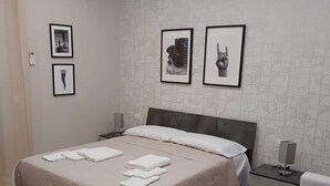 A modern bedroom with a large bed, a bedside table, a gray sofa, and wall art. - Torre del Greco waterfront apartment - 6 floor with panoramic view  (Torre del Greco)