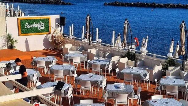 An outdoor café with tables and chairs, a sign reading "Conviviality Club", and a view of the sea and mountains in the background. - Torre del Greco waterfront apartment - 6 floor with panoramic view  (Torre del Greco)