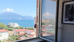 A room with a large window overlooking a coastal town and a mountain. - Torre del Greco waterfront apartment - 6 floor with panoramic view  (Torre del Greco)