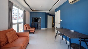 A modern living room with a sofa, a dining table, and a TV. - New Nordic Club 2 by Apartwell (Pattaya)
