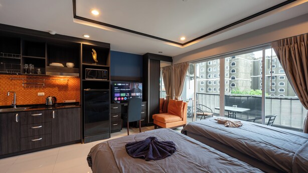 A modern hotel room with a kitchenette, a large bed, a seating area with a view, and a balcony. - New Nordic Club 2 by Apartwell (Pattaya)