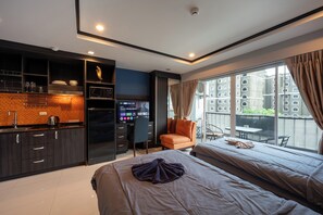 A modern hotel room with a kitchenette, a large bed, a seating area with a view, and a balcony. - New Nordic Club 2 by Apartwell (Pattaya)