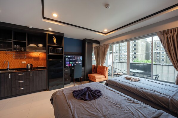 A modern hotel room with a kitchenette, a large bed, a seating area with a view, and a balcony.