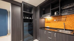 A modern kitchen with dark wood cabinets, a black refrigerator, and a tiled backsplash. - New Nordic Club 2 by Apartwell (Pattaya)