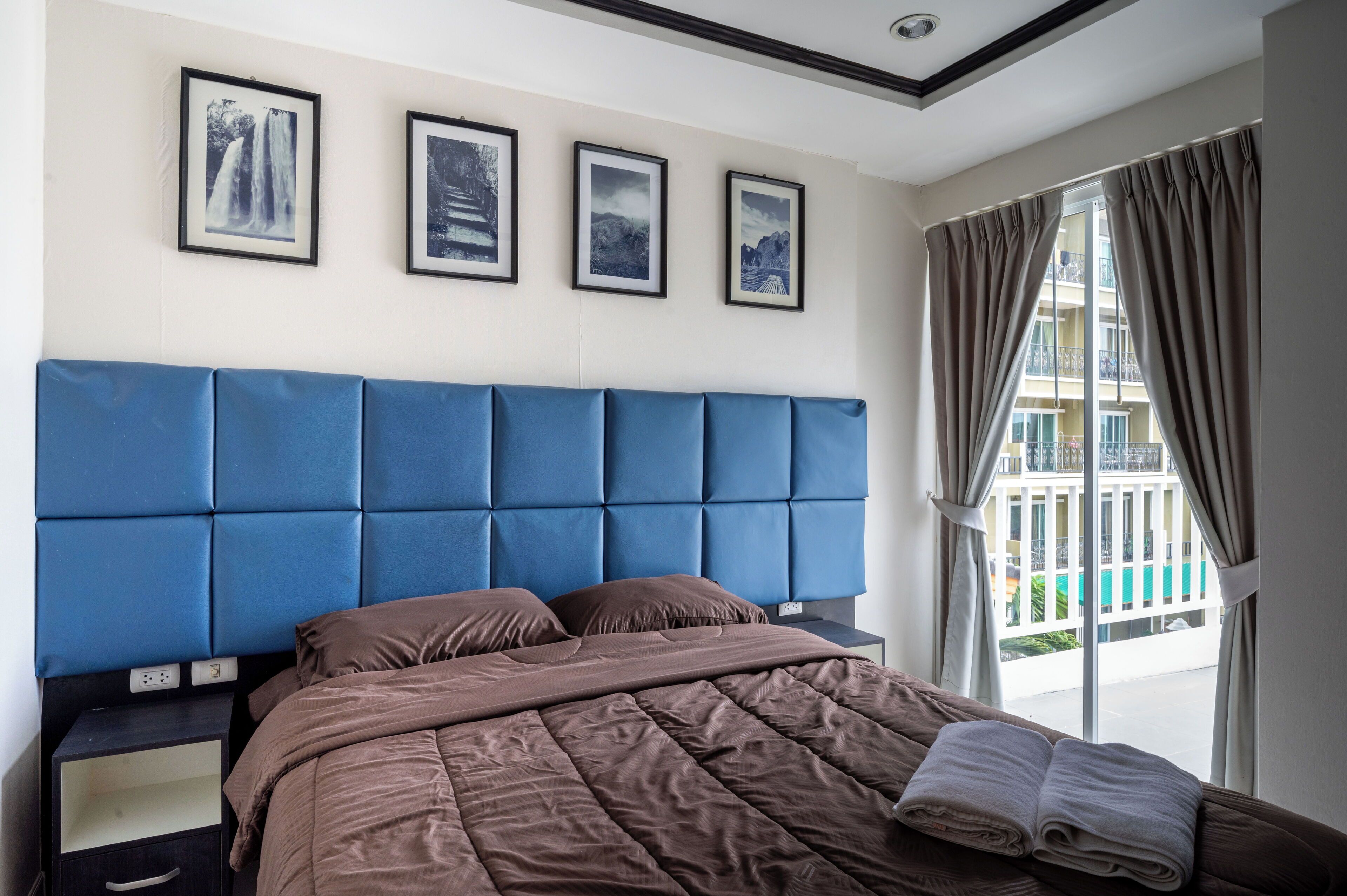 A hotel room with a large bed, a headboard, a nightstand, and a window with curtains.