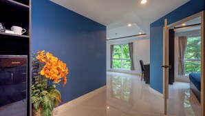 A hotel room with a blue wall, a potted plant, a bed, a desk, and a window with curtains. - New Nordic Club 2 by Apartwell (Pattaya)