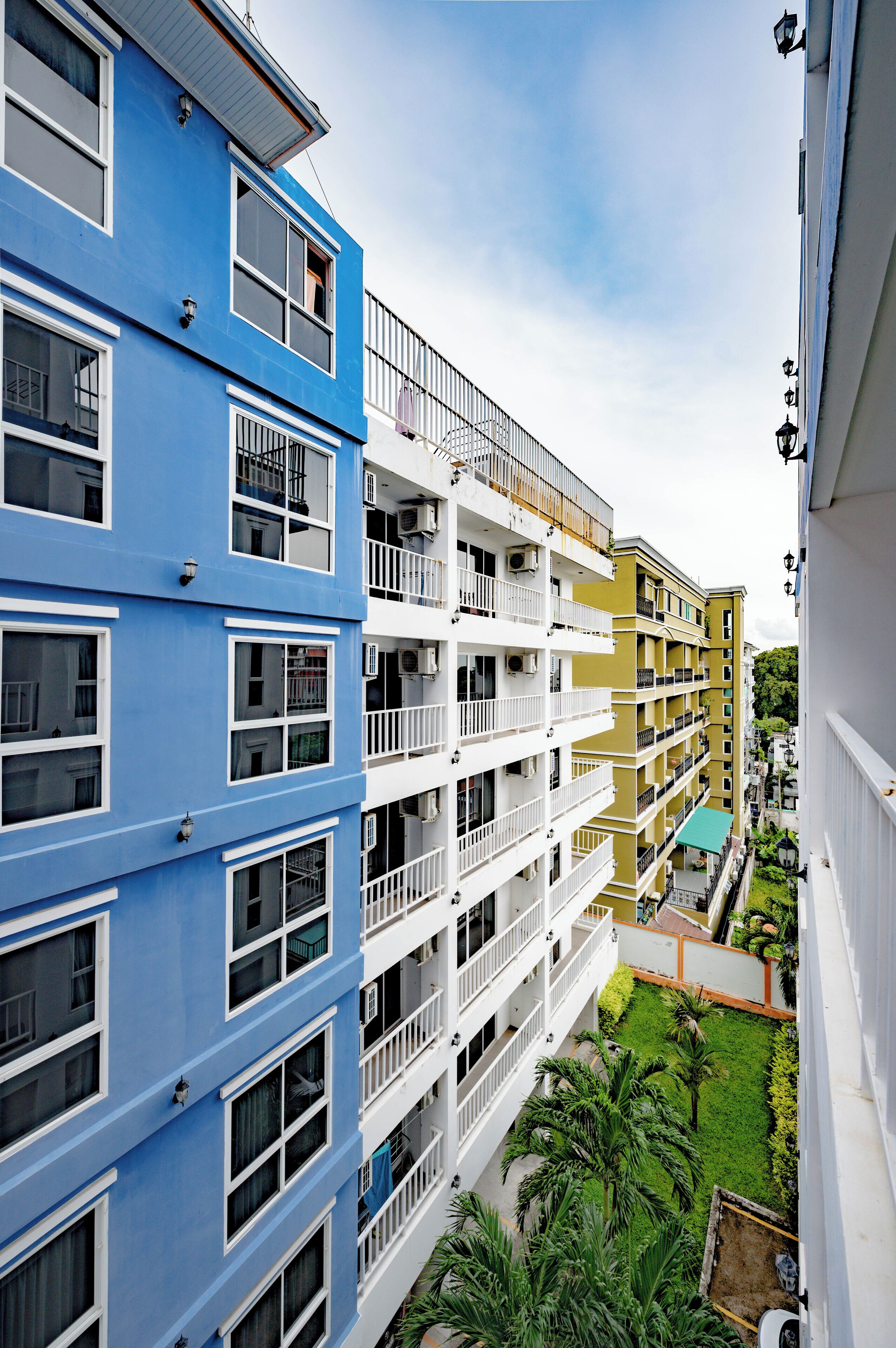 Un edificio residencial de varios pisos con balcones, unidades de aire acondicionado y un pequeño patio con vegetación.