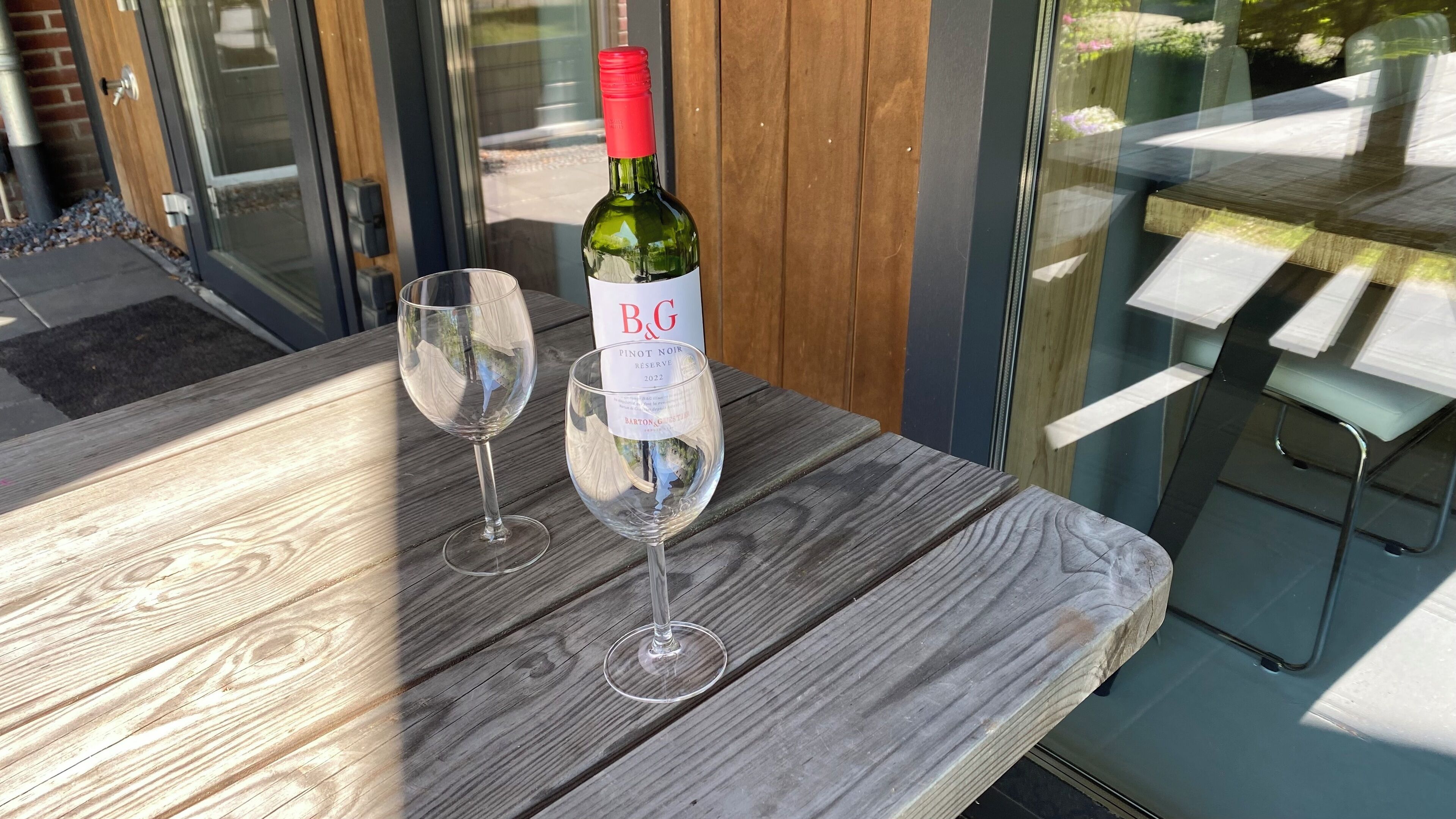 Ett träbord med två vinglas och en flaska B&G Pinot Noir Reserve 2022.