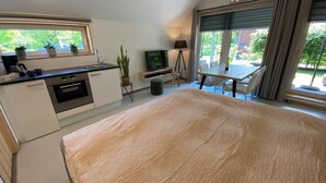 Ett modernt sovrum med en stor säng, en liten köksdel med spis och diskho, en TV och en balkong med ett bord och stolar.