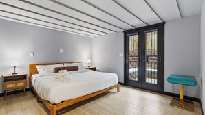 Un dormitorio con una cama de madera, dos mesitas de noche, una mesita auxiliar y una ventana con vistas, además de una mesita lateral azul turquesa.
