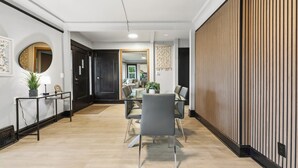 Un interior moderno con comedor que incluye una mesa de vidrio y sillas, un espejo redondo y un panel de pared de madera.