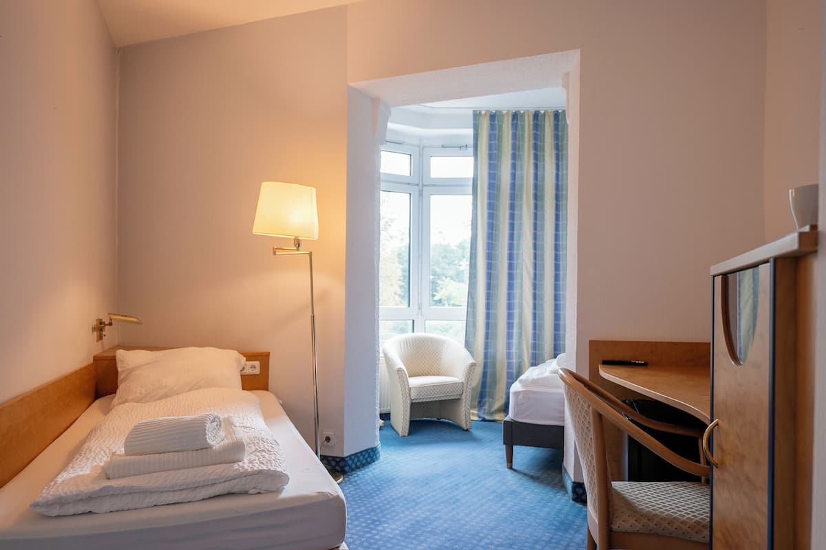Habitación de hotel con cama, escritorio, silla, lámpara y vistas al exterior.