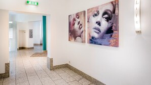 Un couloir avec une enseigne de sortie verte, un luminaire et deux œuvres d’art accrochées au mur.
