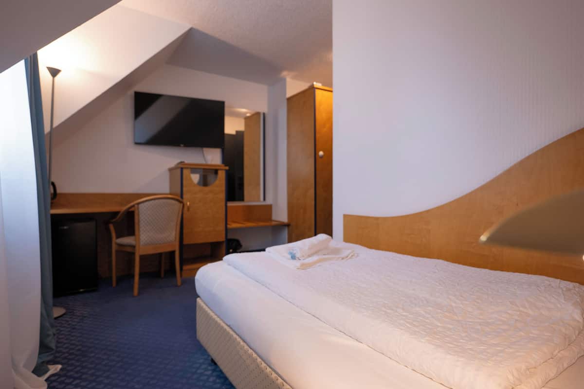 Una habitación de hotel con cama, escritorio, silla, televisor y armario.