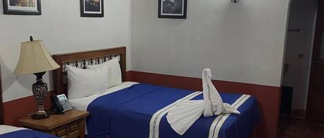 A hotel room with two beds, a wooden ceiling, a wall-mounted phone, and framed pictures.