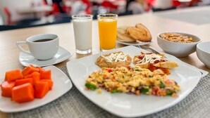 Una mesa de desayuno con platos de comida, una taza de café, un vaso de leche y un vaso de zumo de naranja.