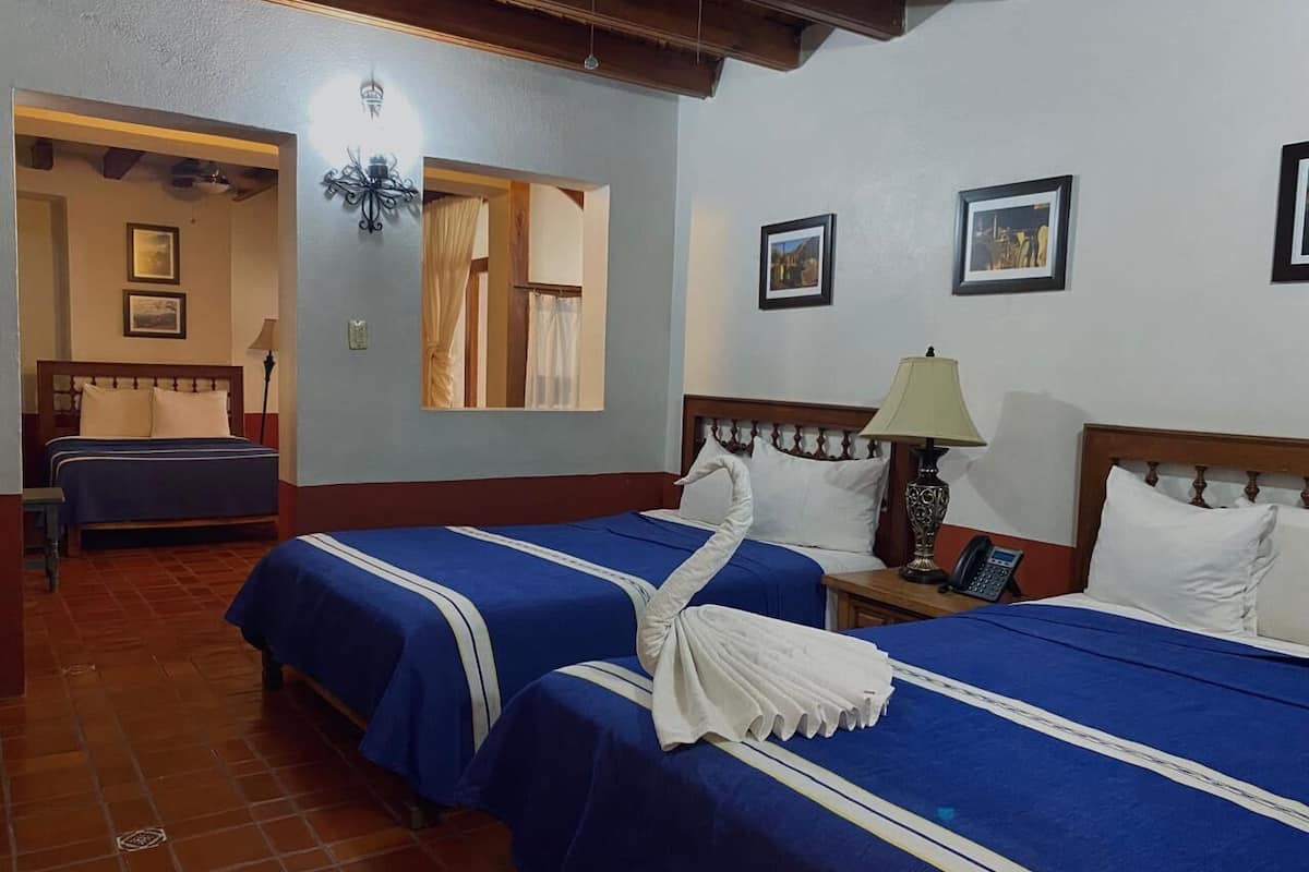 Quarto de hotel com duas camas, cabeceira de madeira, mesa de cabeceira com abajur e telefone.