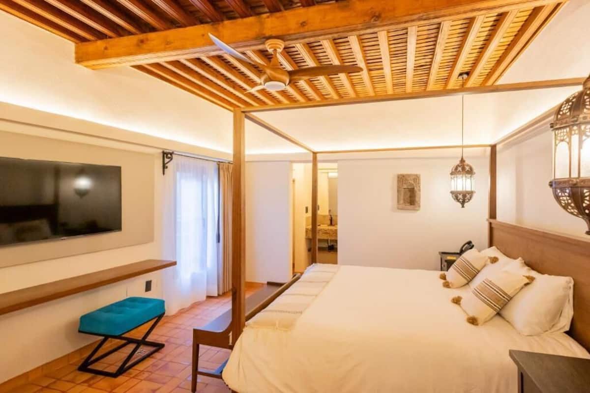 Quarto com cama, televisão na parede, ventilador de teto e mesa de cabeceira com abajur.