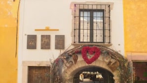 Un edificio con un arco central, una ventana con rejas y un adorno con forma de corazón.