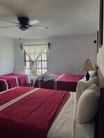 Una habitación con dos camas individuales, un ventilador de techo, una ventana con cortinas y una lámpara de noche.