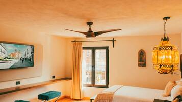 Habitación de hotel con dos camas, un ventilador de techo, un televisor en la pared, una ventana con cortinas y una lámpara colgante.