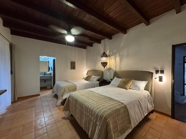 A hotel room with two beds, a ceiling fan, a light fixture, and a door.