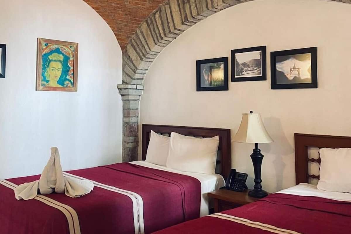 Quarto de hotel com duas camas, um ventilador de teto e uma parede de tijolos.