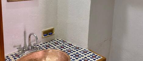 A bathroom with a copper sink, a mirror, a wooden cabinet, and a black hanger on the wall.
